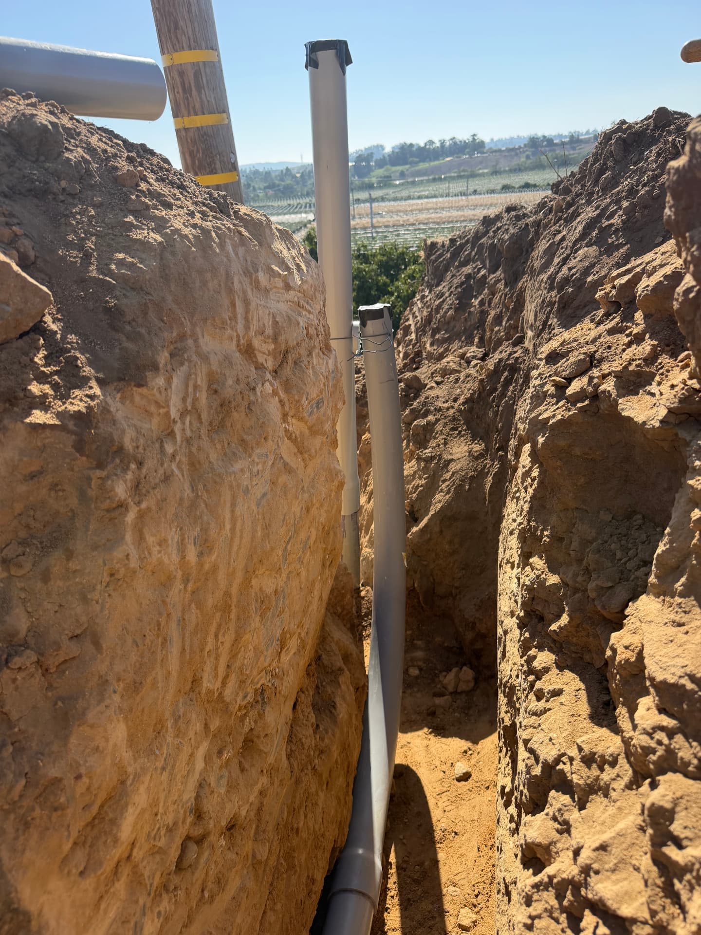 Conduit running along an excavated trench and turning upward beside a wooden utility pole